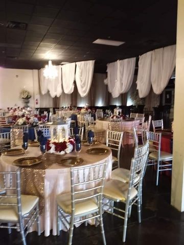 Decorated banquet hall with round tables, silver chairs, and white draped ceiling decor