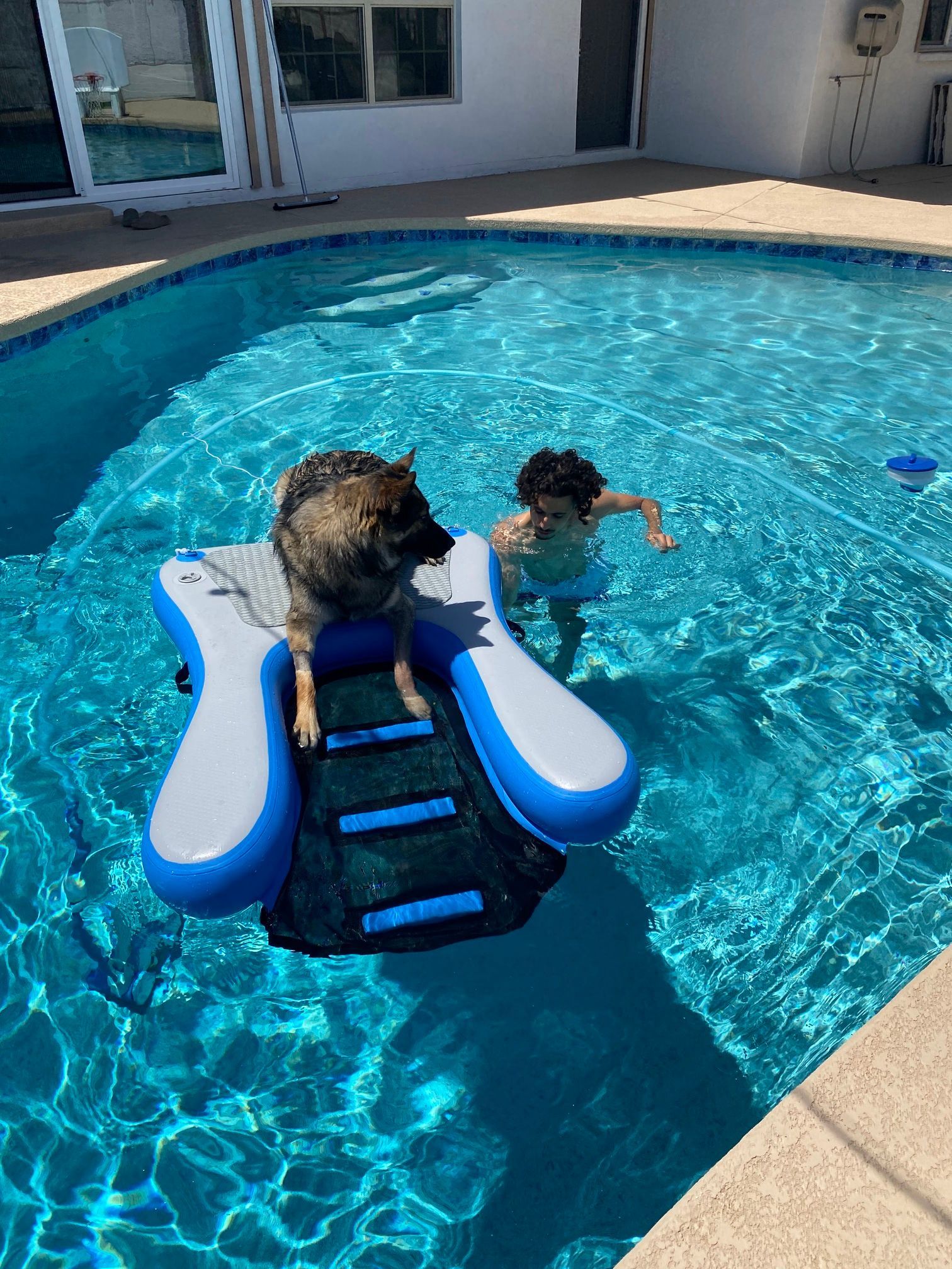 Child in a blue pool float facing a child swimming in a backyard pool