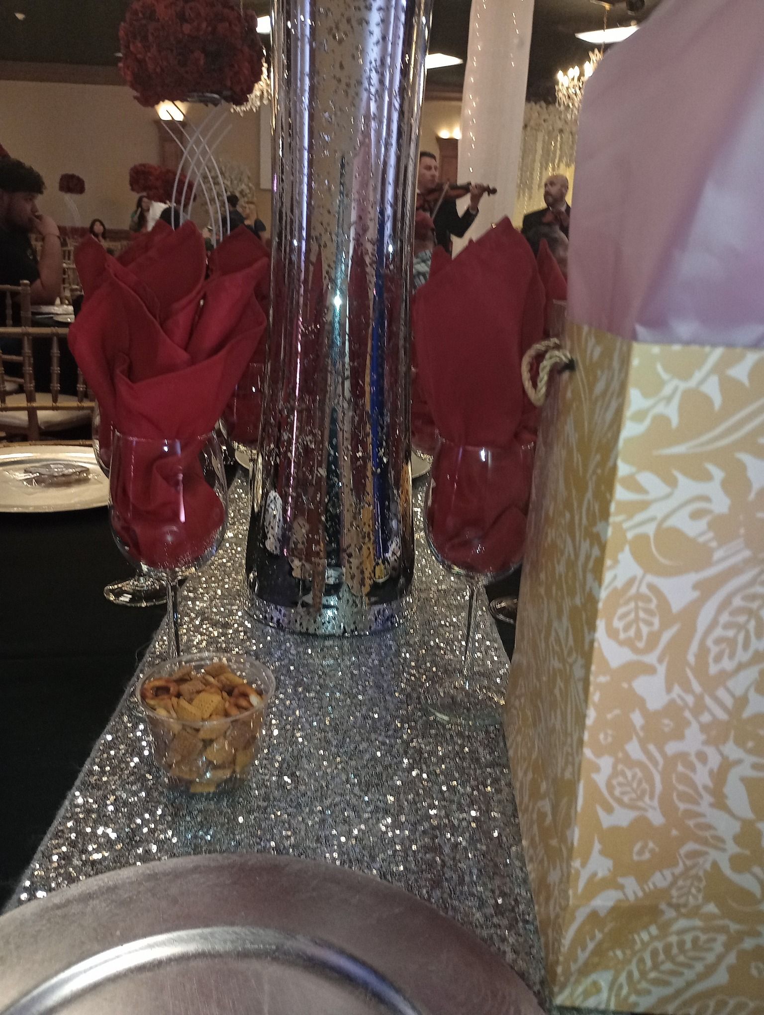 Sparkling table centerpiece with red napkins, a mirrored vase, and a gold patterned gift box on a banquet table