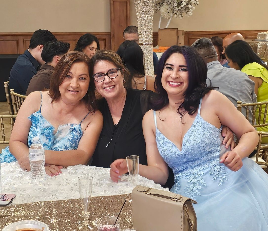 Three women in light blue dresses smile at a decorated banquet table at a formal event.