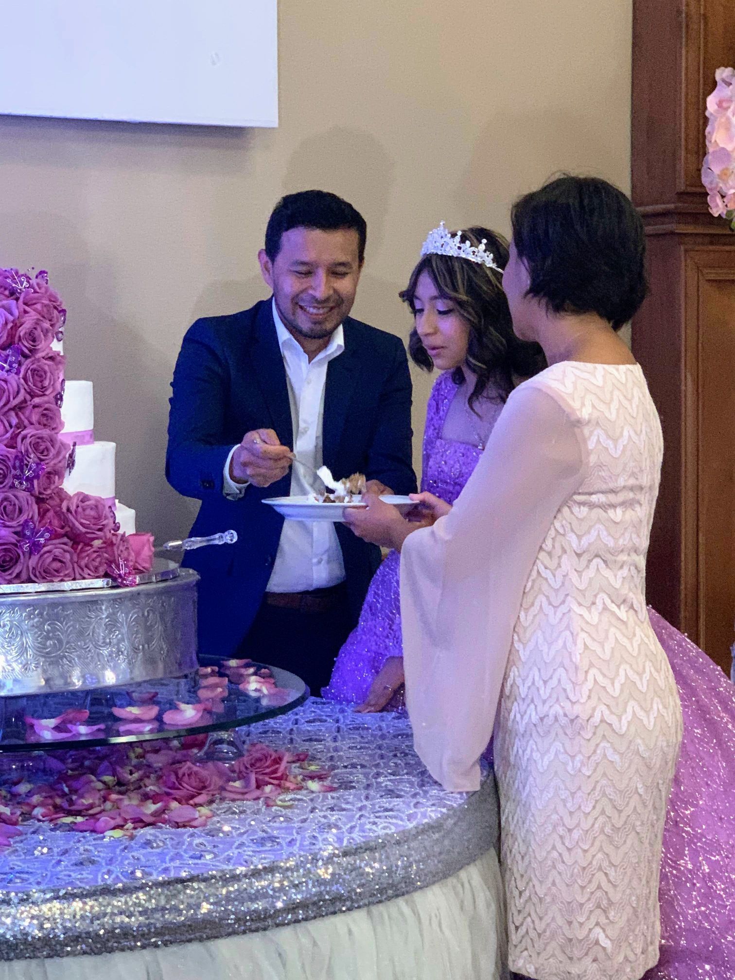 Wedding guests sharing cake beside a pink floral tiered cake at a sparkly dessert table.