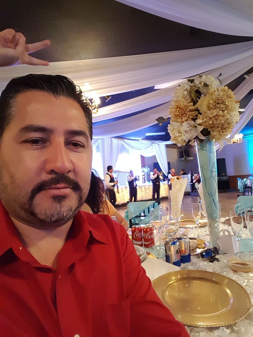 Man in a red shirt at a decorated banquet table with flowers and drinks at a reception venue