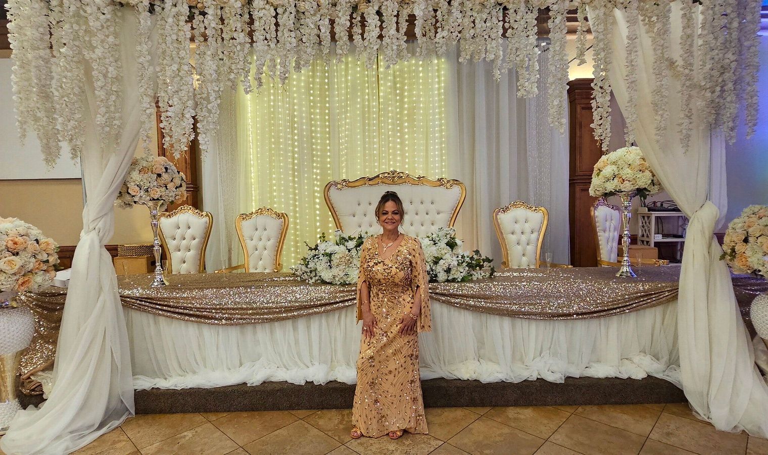 Elegant banquet stage with white drapery, floral decor, and a woman in a gold dress standing center stage.