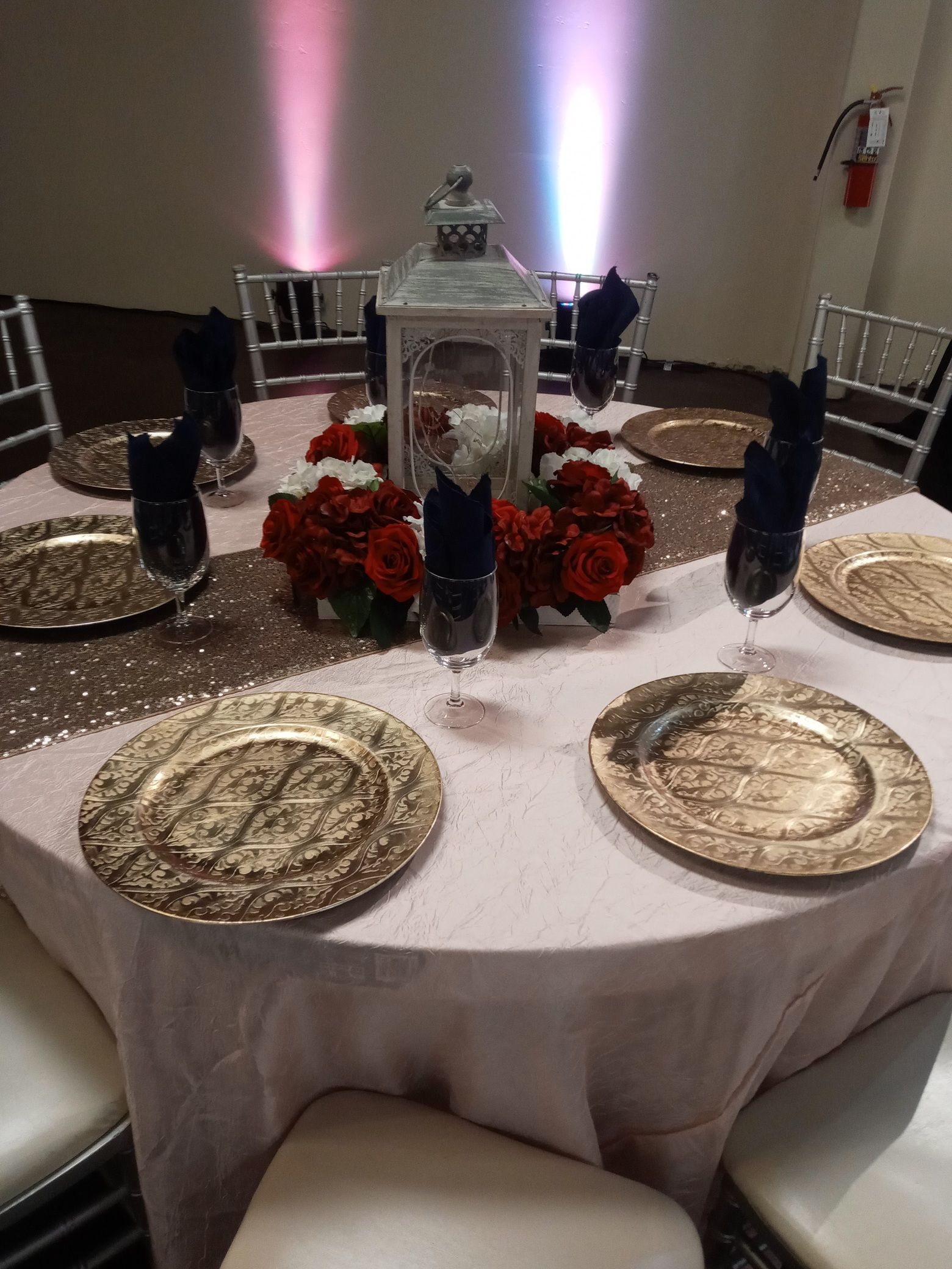 Elegant banquet table with gold plates, red roses, black napkins, and lantern centerpieces in a softly lit hall