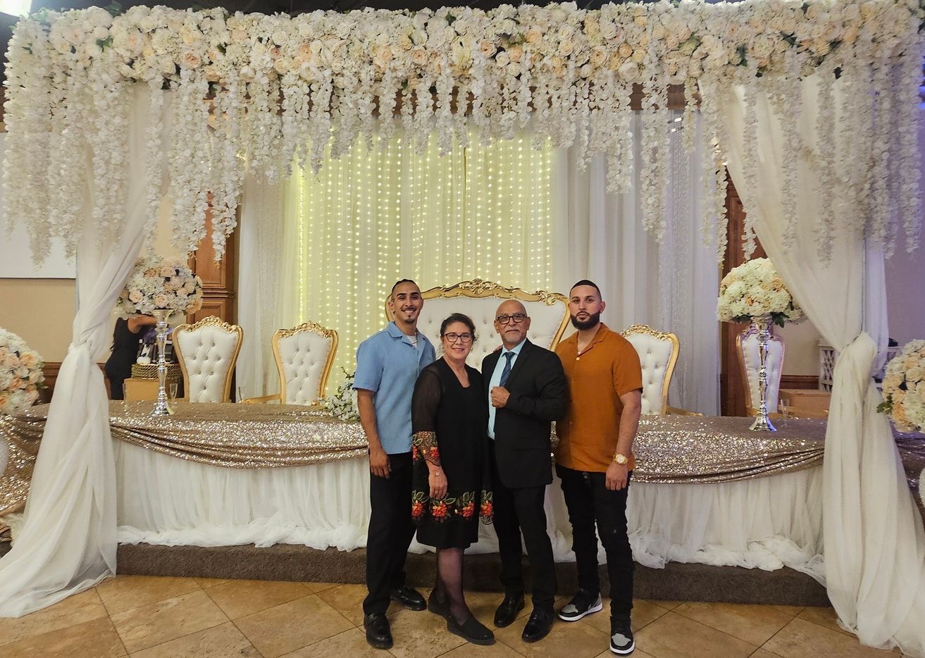Four people posing in front of a floral wedding backdrop and decorated dessert table
