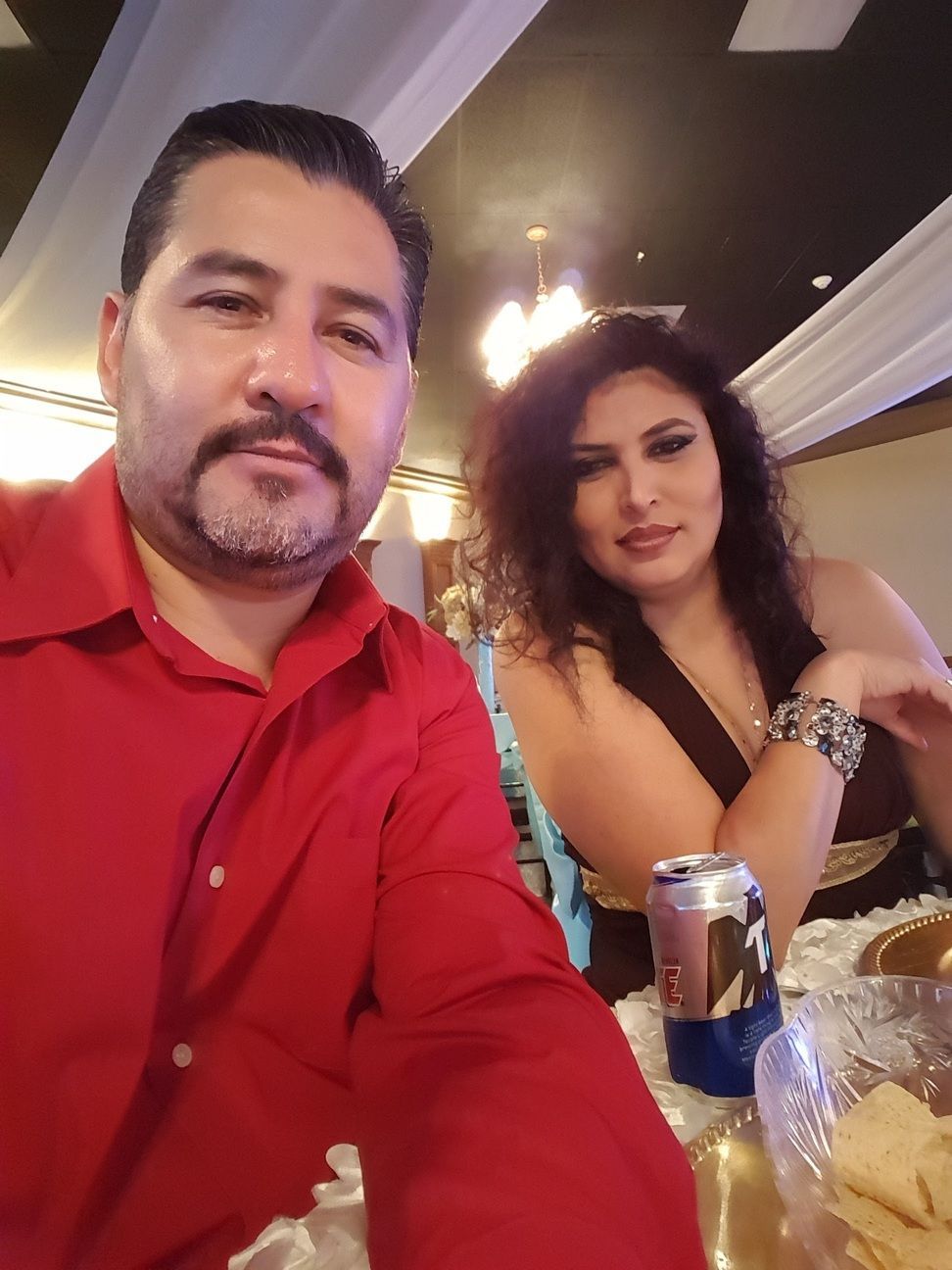Two people seated at a table in a dimly lit restaurant, one in a red shirt and one in a black dress.