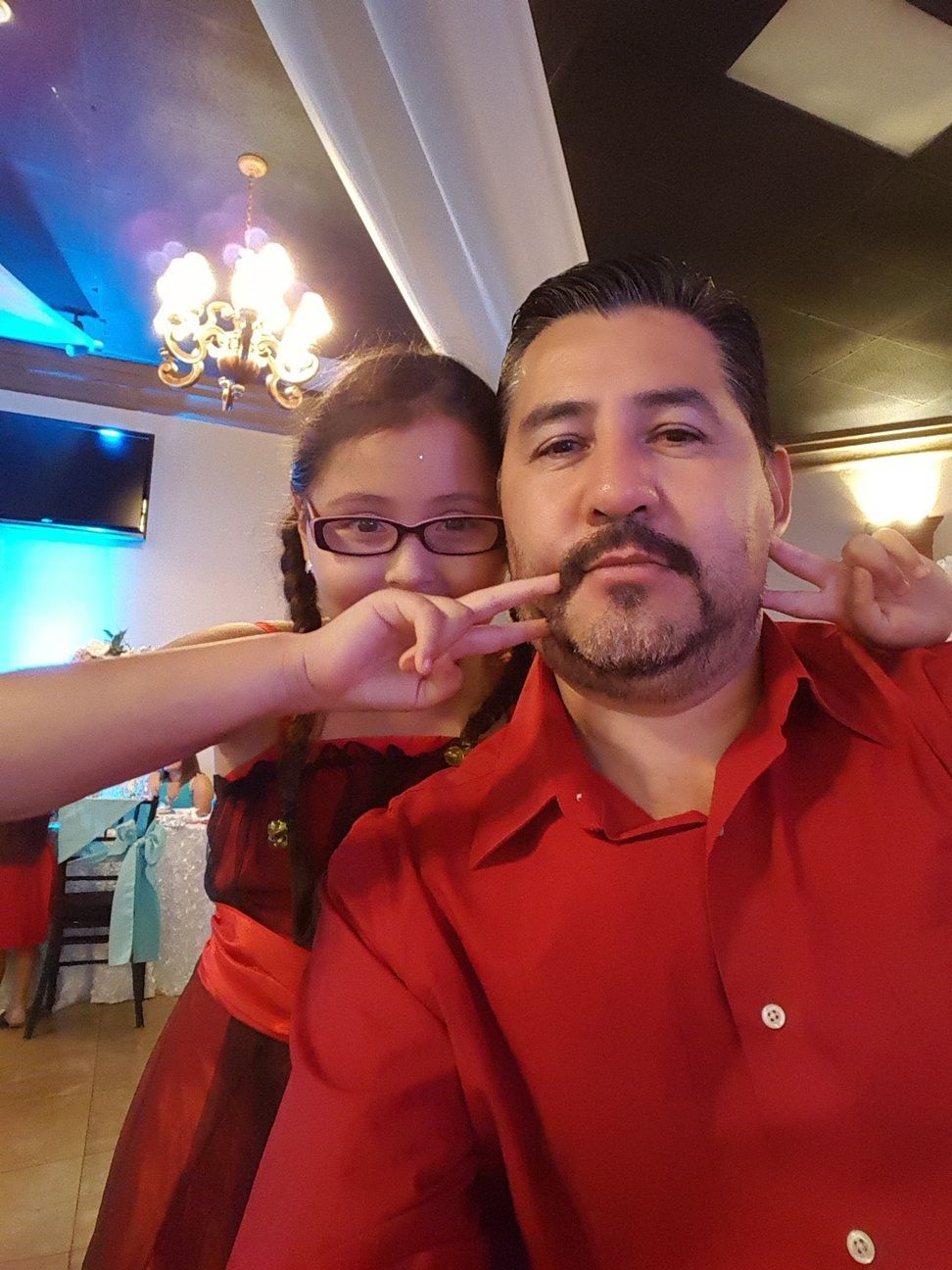 Two people in a restaurant, one in a red shirt while the other playfully pinches his cheeks.