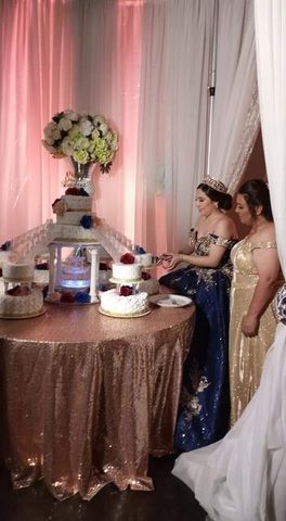 Two women in formal gowns standing beside a decorated dessert table at a pink-lit party backdrop