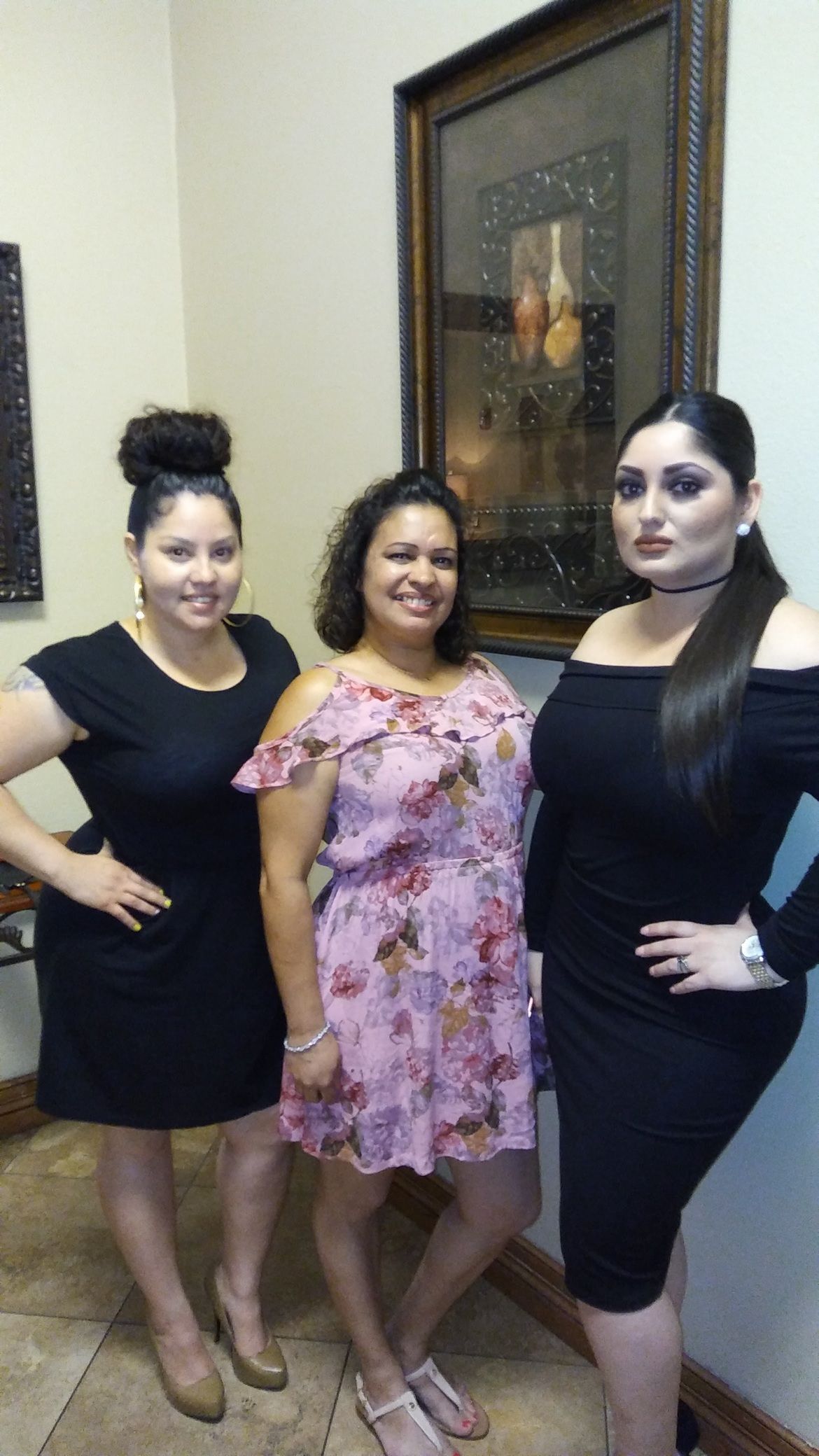 Three women posing indoors, with one in a pink dress and two in black dresses.