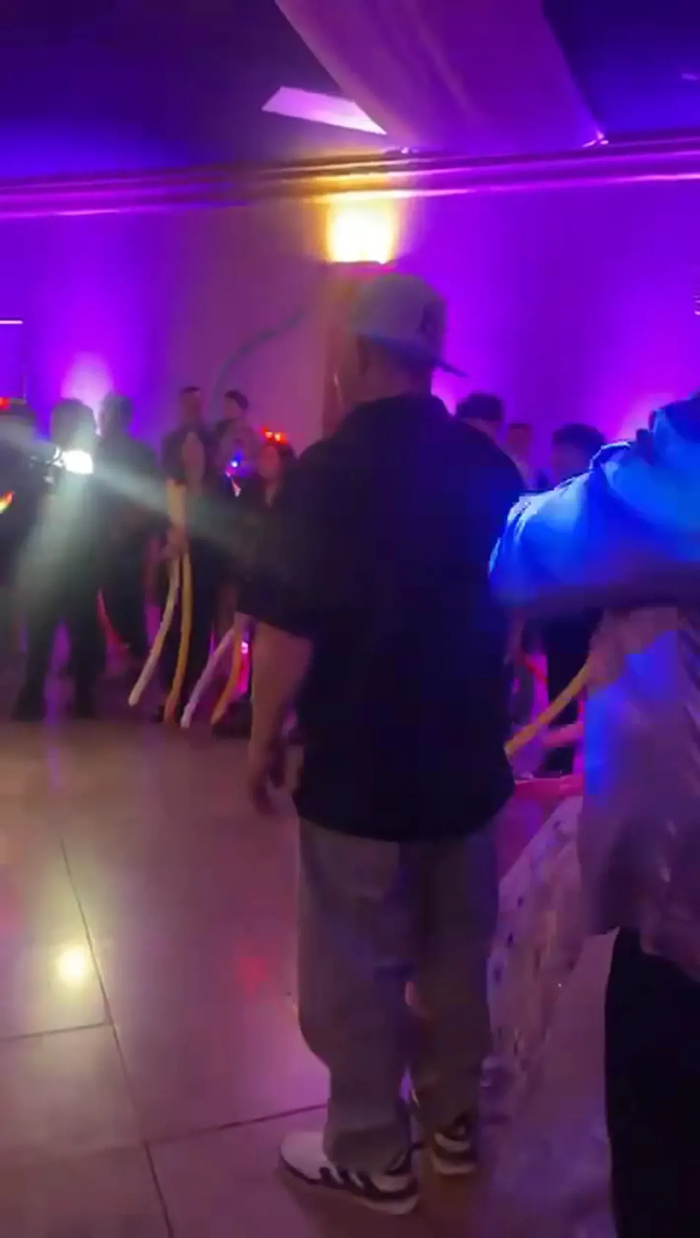 People dancing in a purple-lit room at a party, with one person in a beanie in the foreground