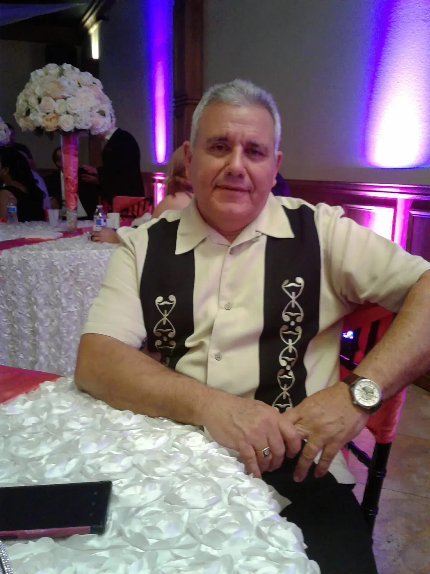Man seated at a decorated banquet table with purple lighting and a white floral centerpiece