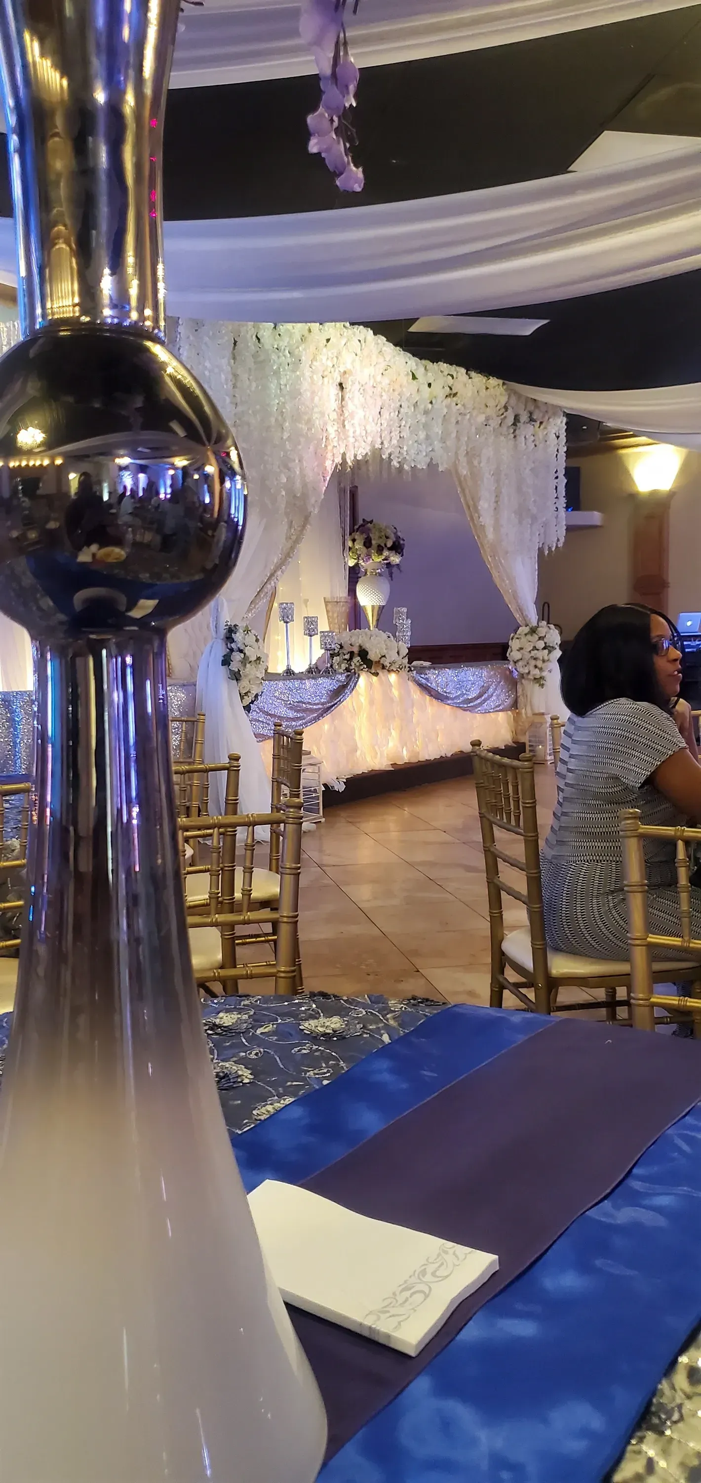 Elegant event hall with blue and gold decor, banquet tables, and a mirrored column in the foreground