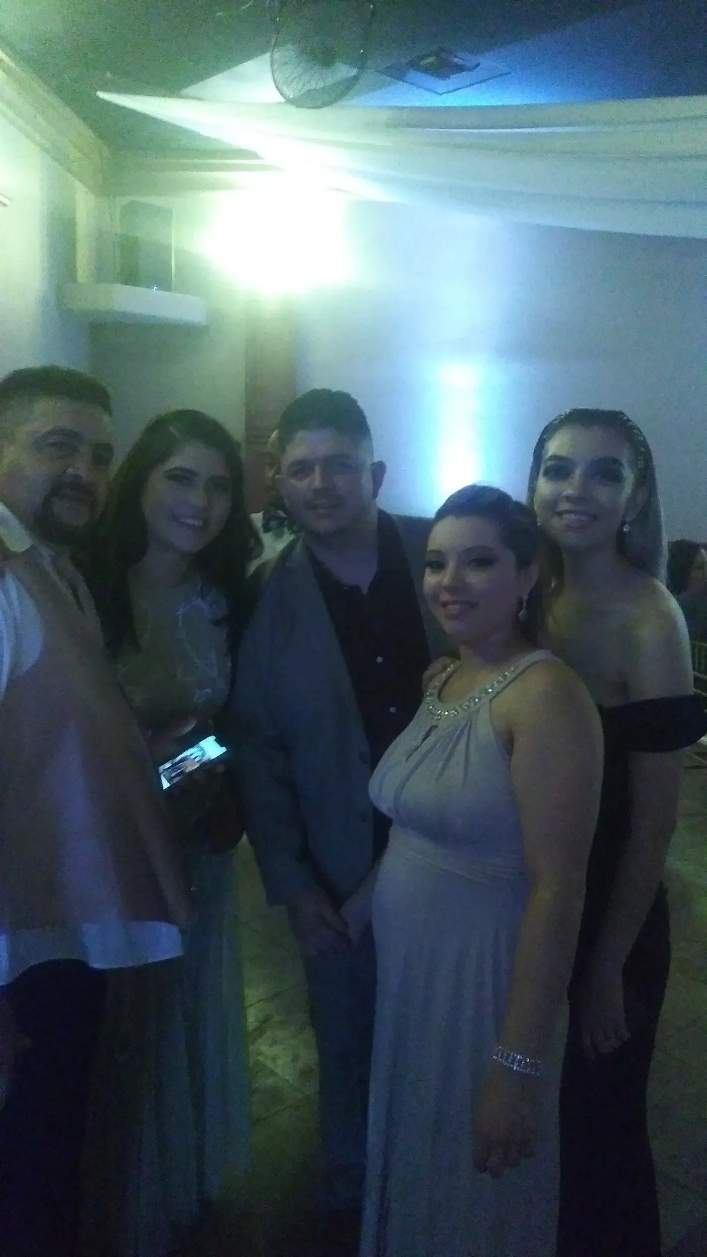 Five people posing at a dimly lit indoor party, with blue and green lights behind them.