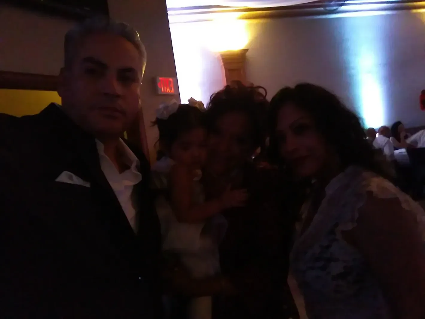 Four people posing together in a dimly lit indoor event space, with a bright light in the background