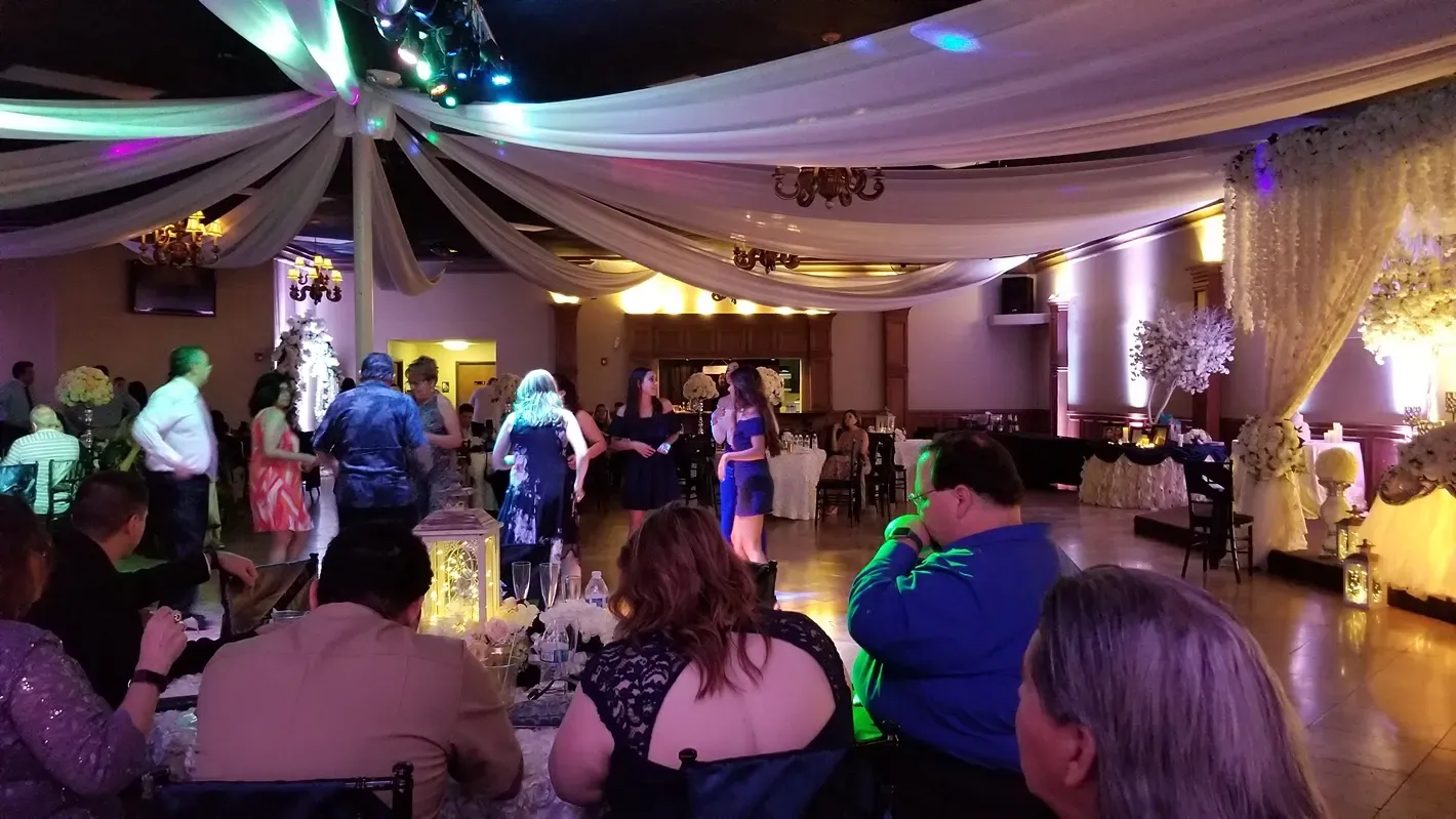 People seated in a decorated banquet hall with colorful lighting, watching a social event.