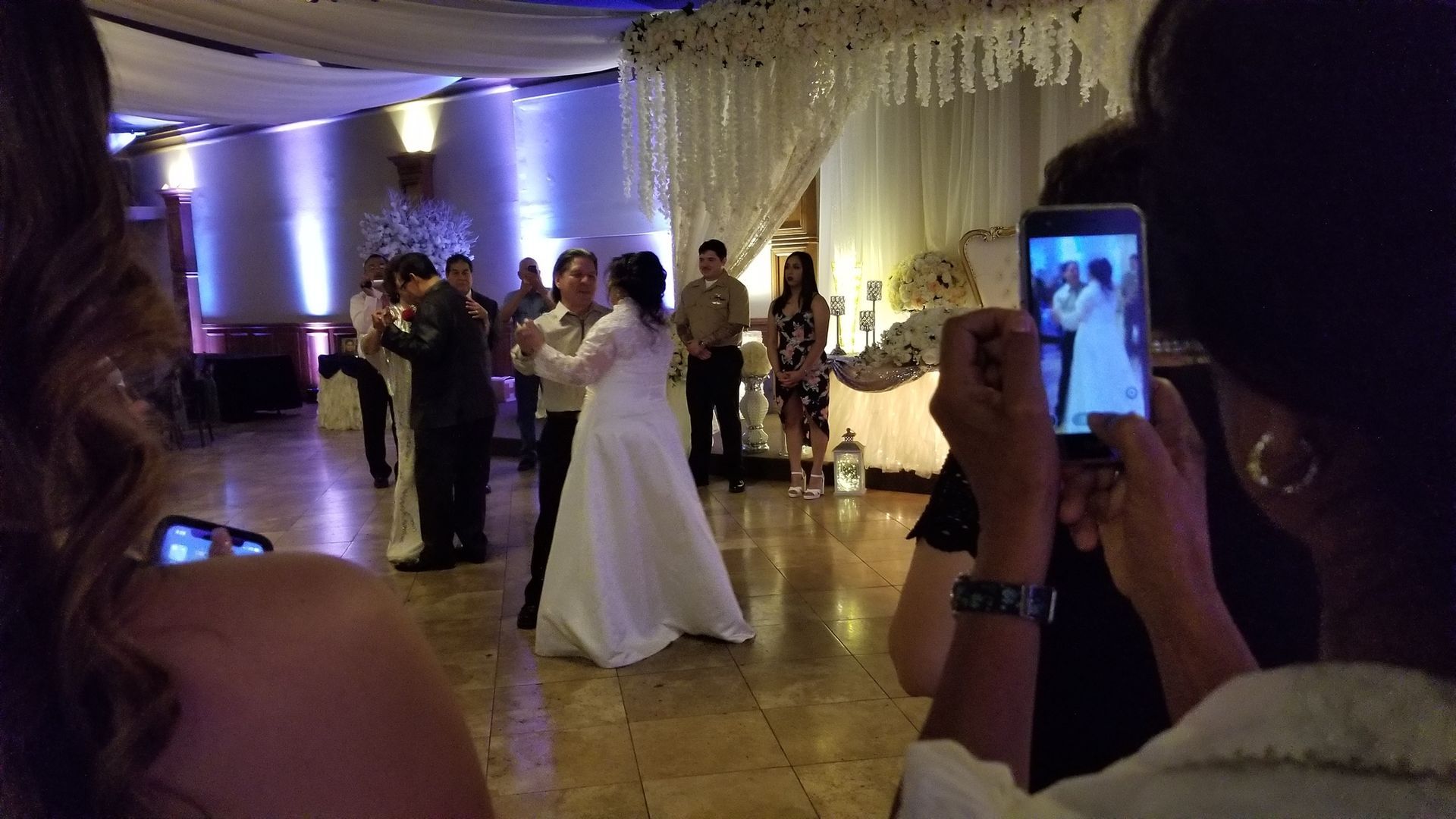 Bride and groom dancing at a wedding reception while guests record on their phones