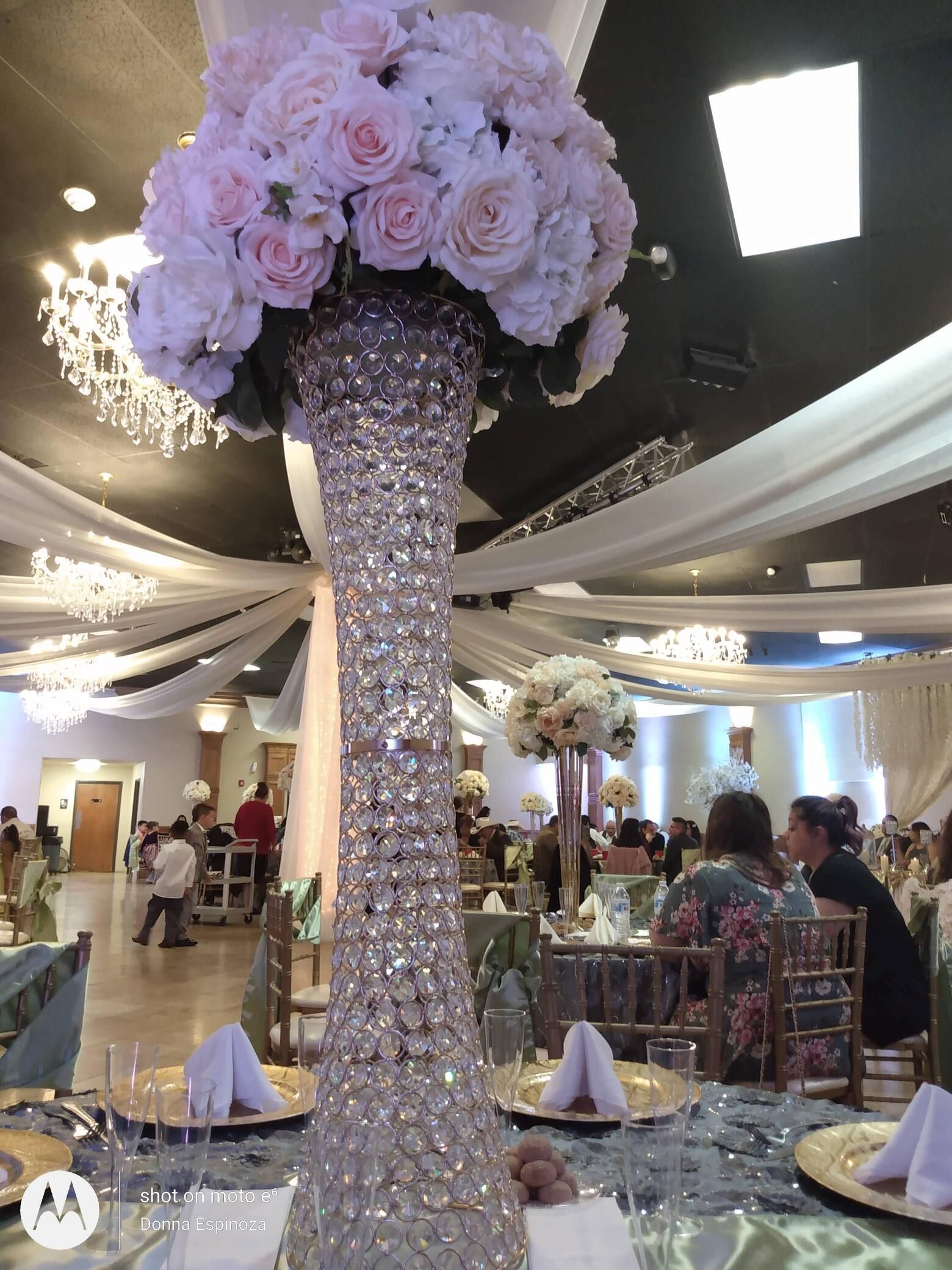 Tall crystal floral centerpiece with pink and white roses in a decorated banquet hall