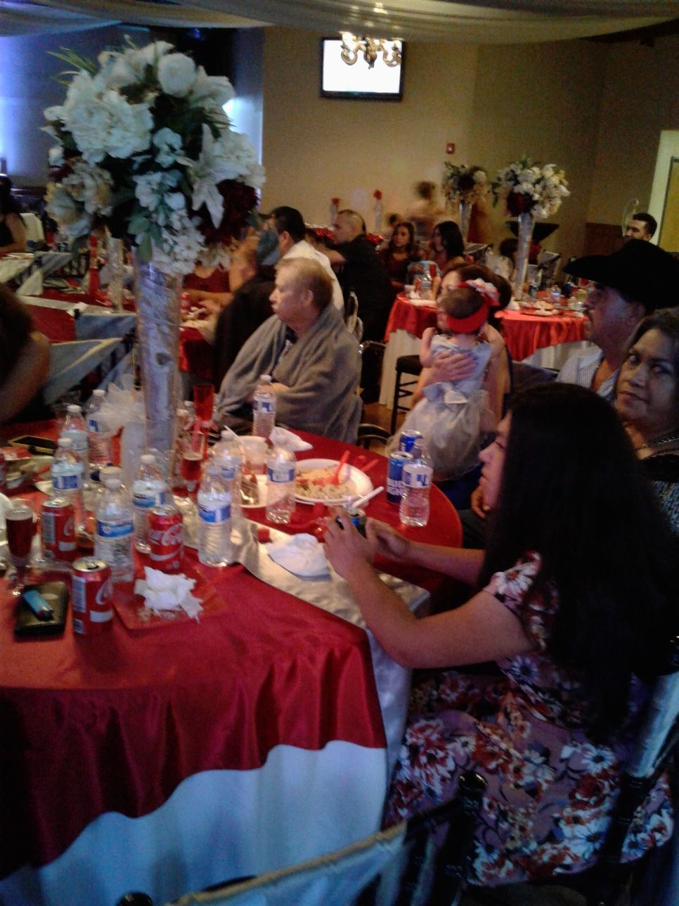 People seated at a red tablecloth-covered banquet table with drinks and flowers at an indoor event.