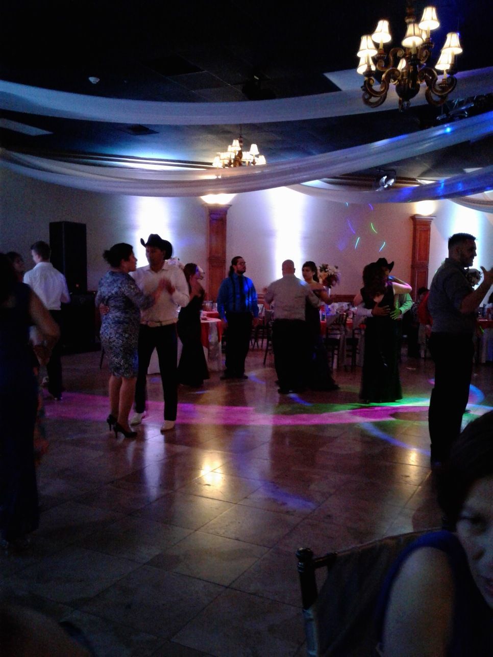 People dancing at a dimly lit banquet hall with chandeliers and colorful floor lights