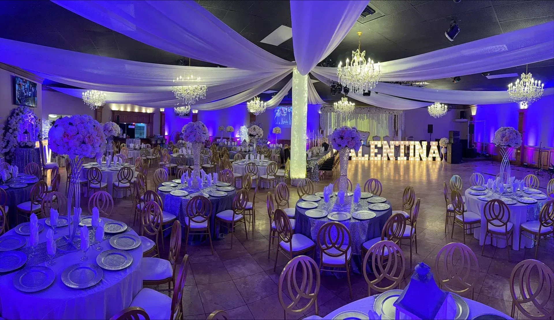Elegant banquet hall with round tables, white drapery, and purple-blue uplighting for an event