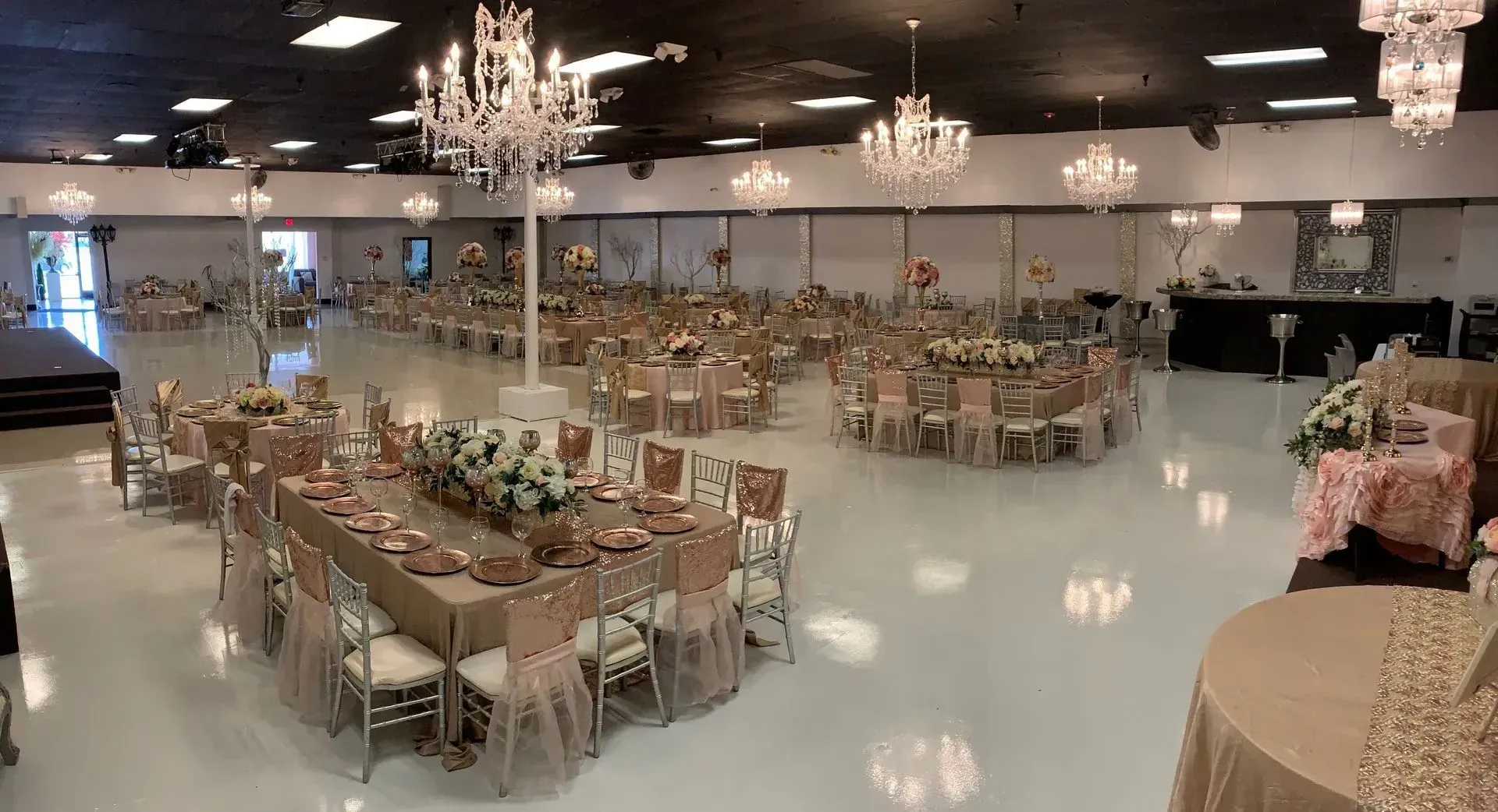 Decorated banquet hall with round tables, floral centerpieces, and chandeliers on a glossy floor