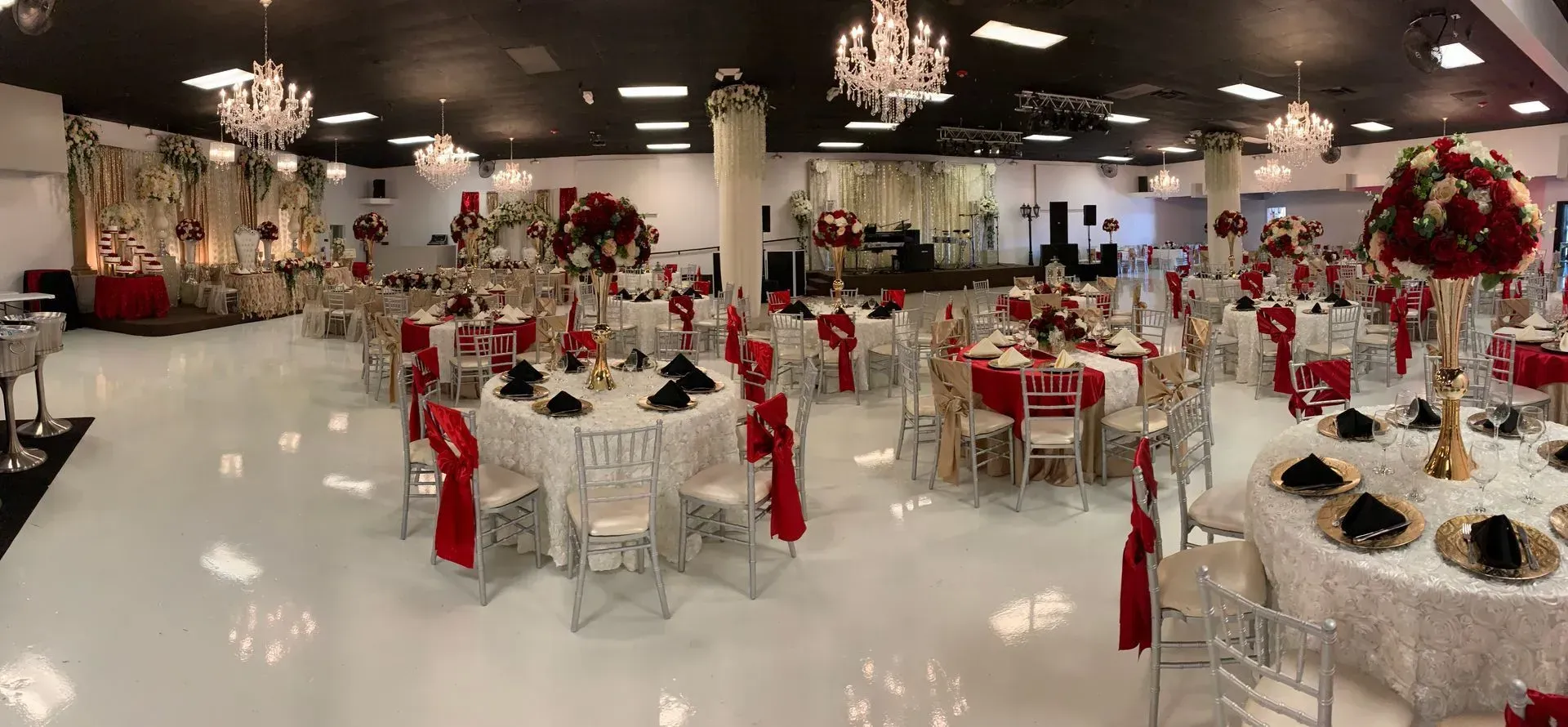 Elegant banquet hall with white tables, red chair sashes, chandeliers, and floral centerpieces