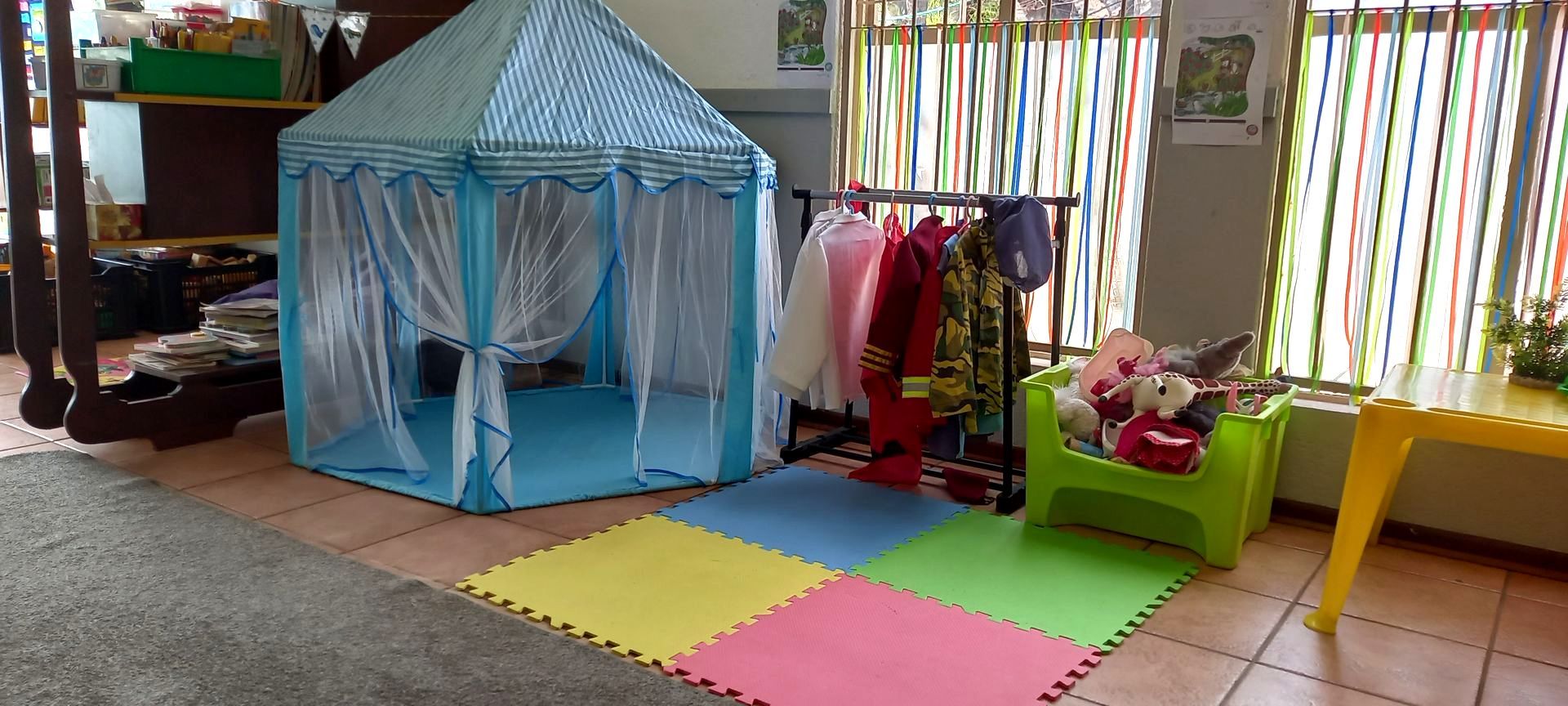 A play tent, dress-up clothes, and toys are in a colorful indoor playroom.