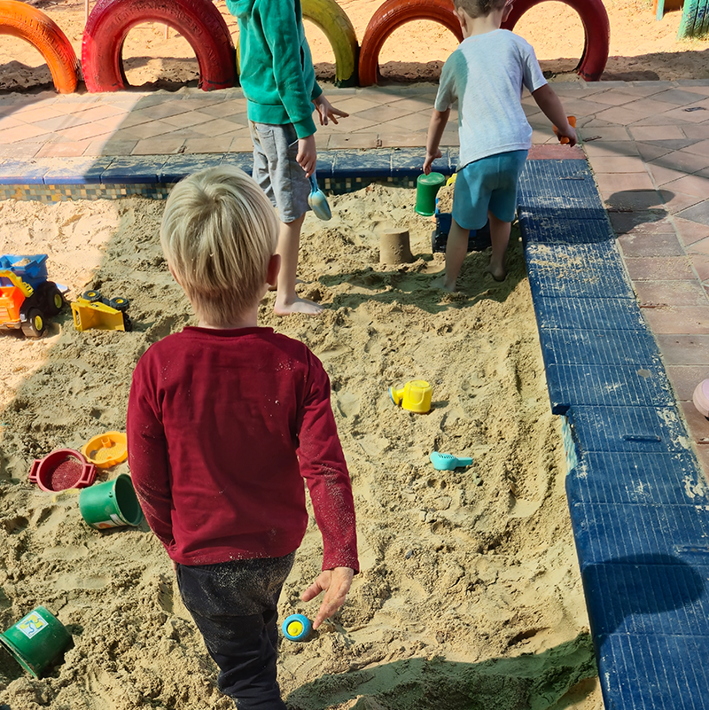 Children playing in a sandbox with toys; colorful tires border the play area.