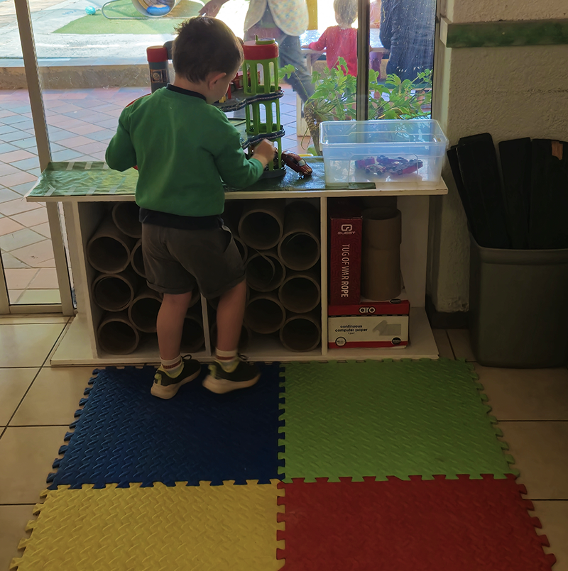 Boy playing with toys at a table with cardboard tubes; colorful floor mats.