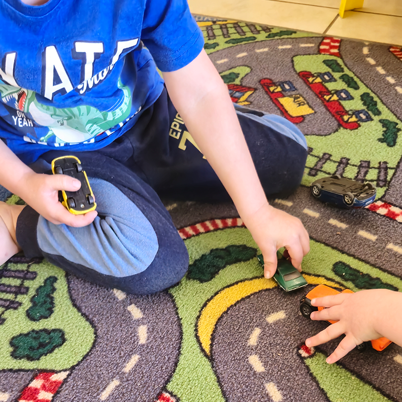 Child playing with toy cars on a road-themed rug.