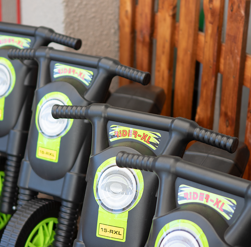 Black and green toy ride-on scooters lined up outdoors with wooden slats in the background.
