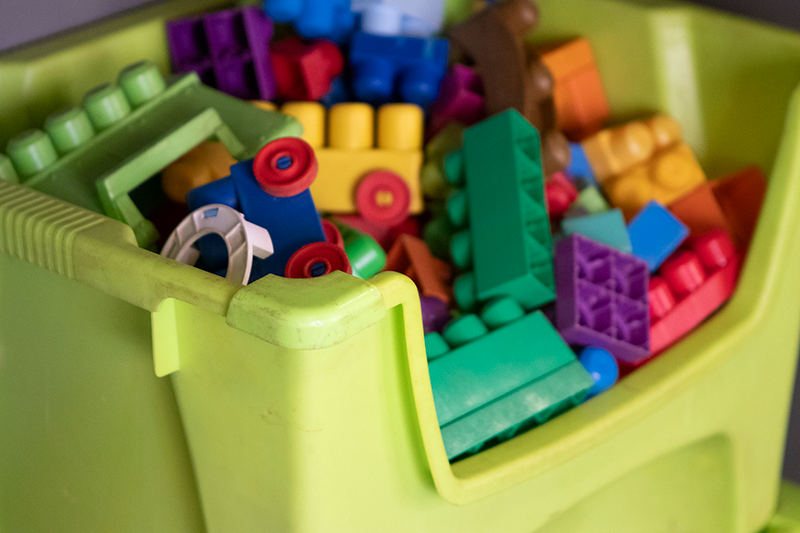 Green toy bin overflowing with colorful building blocks.