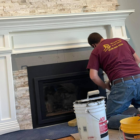 Person painting a fireplace surround white, stone and black details visible.