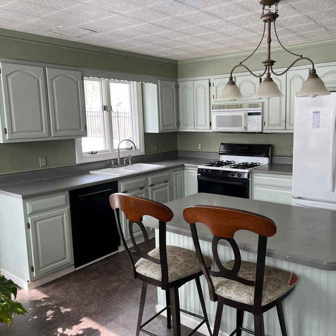 Kitchen with pale green cabinets, gray countertops, and a white refrigerator. Two barstools at the island.