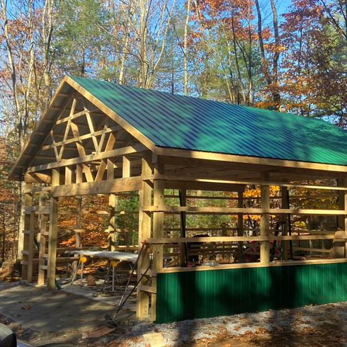 Wooden structure with green roof under construction in a wooded area.