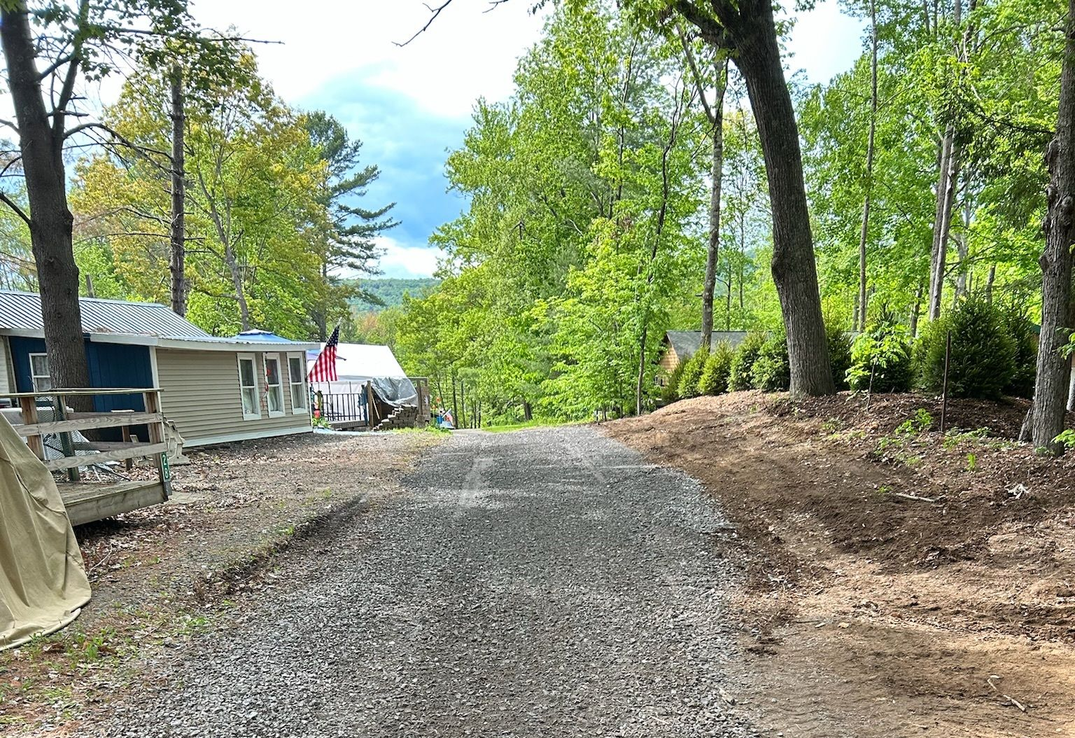 Gravel driveway between cabins and trees under a partly cloudy sky