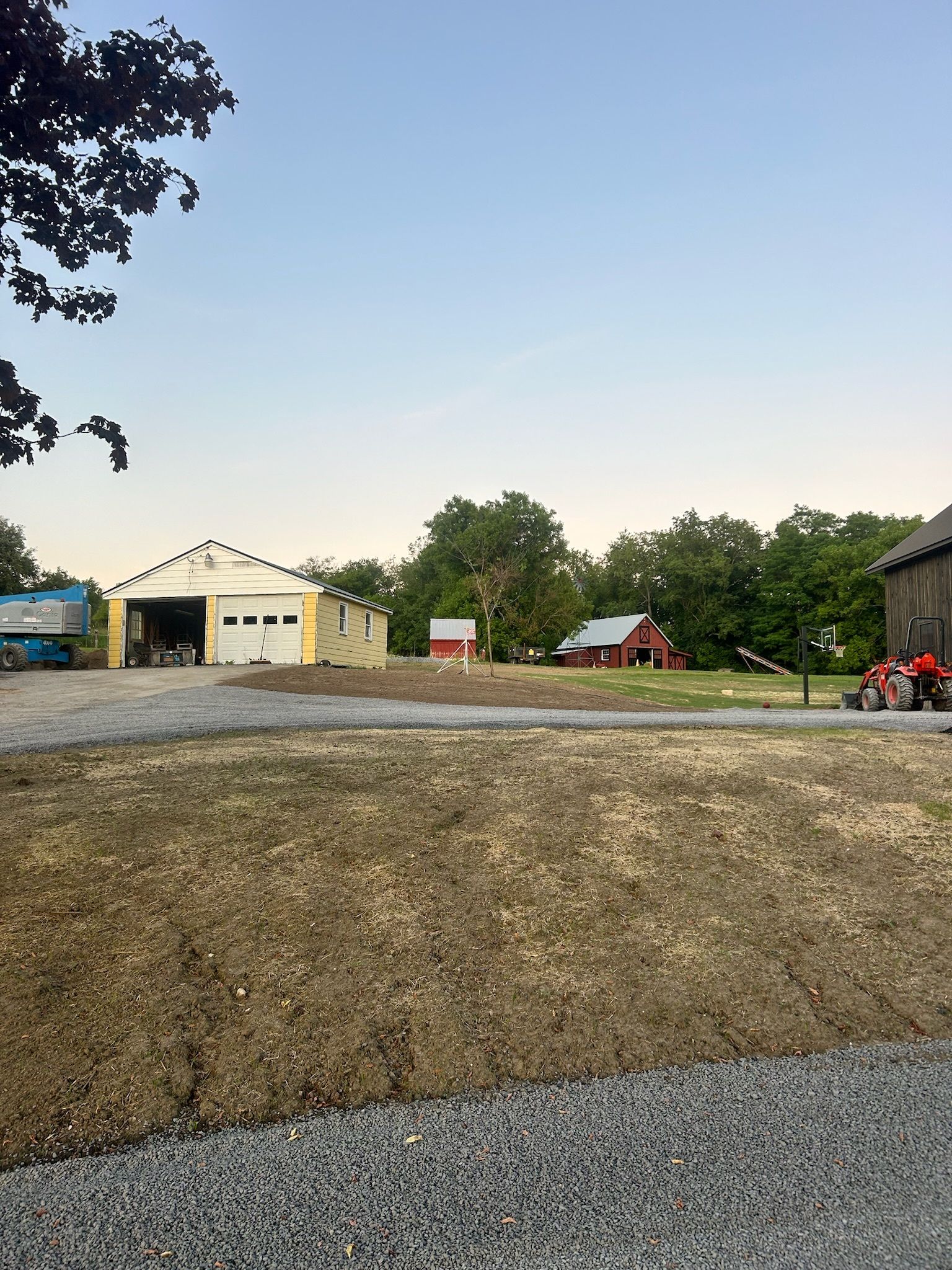 Gravel lot with tents and a white building at dusk, trees and parked vehicles in the background.