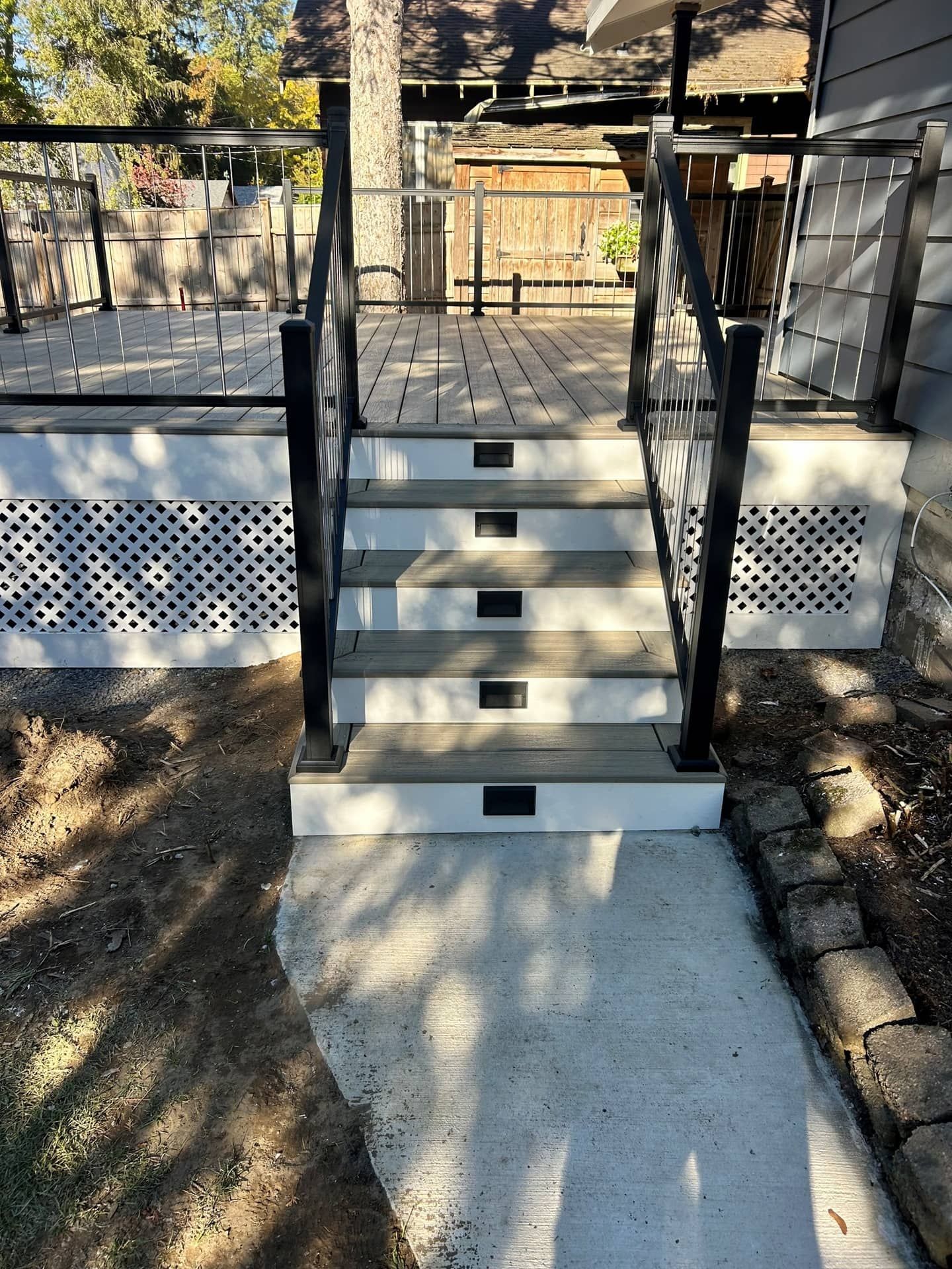 Front steps with black railings leading to a raised porch with lattice skirting in a wooded yard.