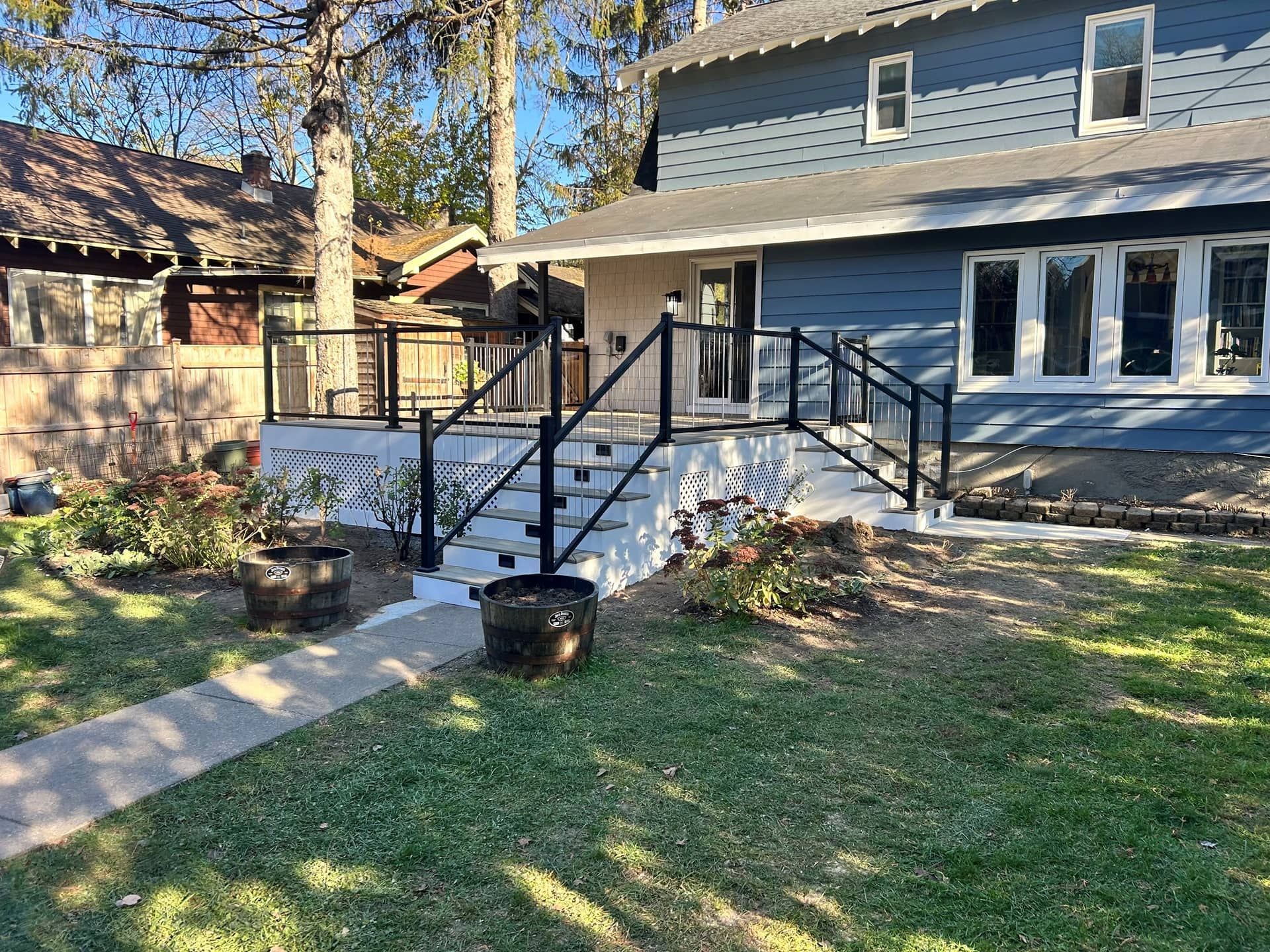 Backyard view of a gray house with white porch railings, black steps, and a grassy yard
