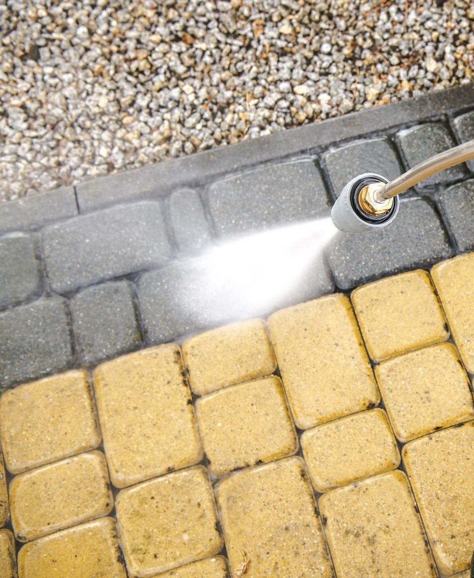 A person is cleaning a brick walkway with a high pressure washer.