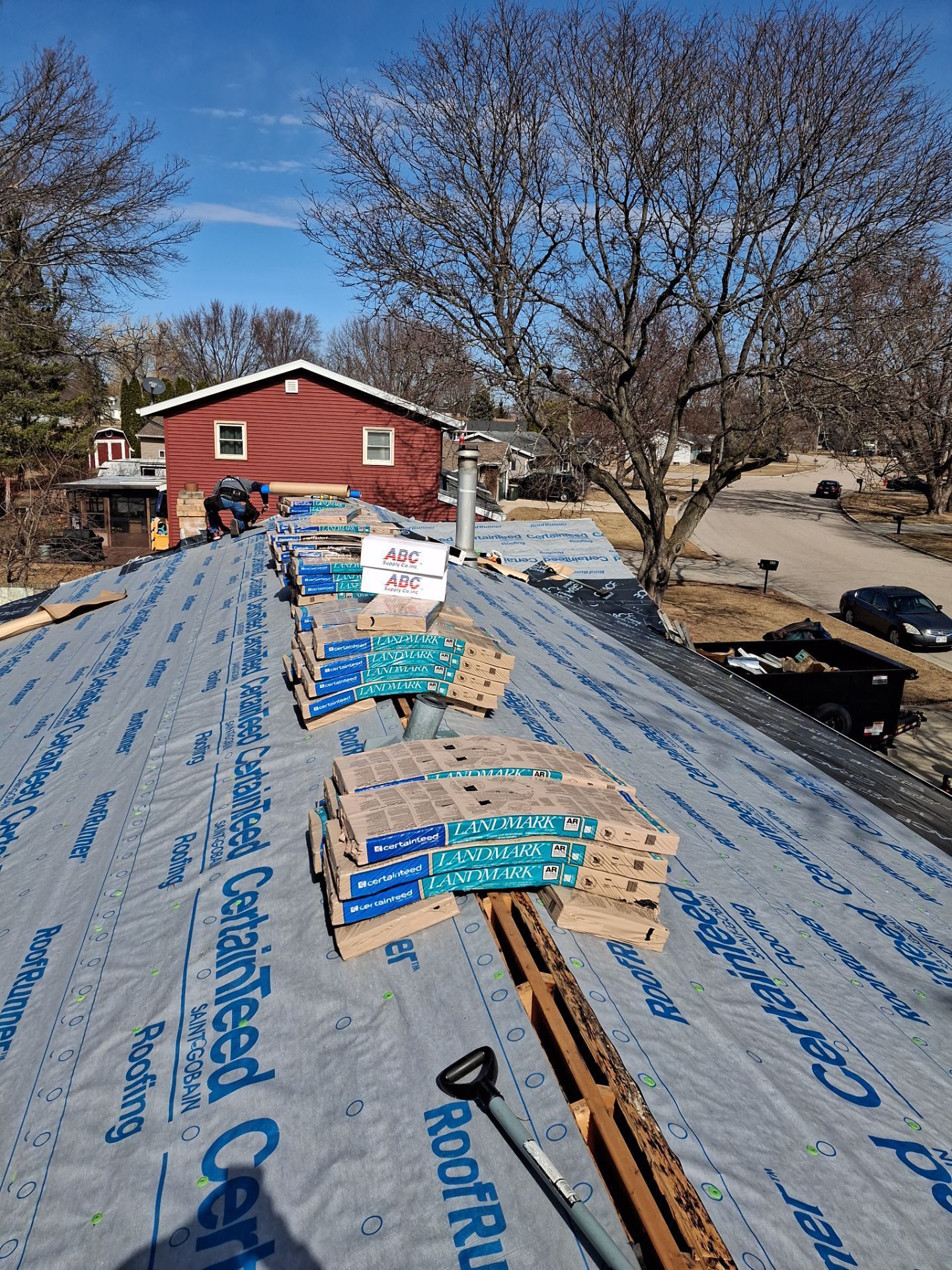 Roofing work in progress: bundles of blue/gray shingles on a roof, covered with roofing underlayment.