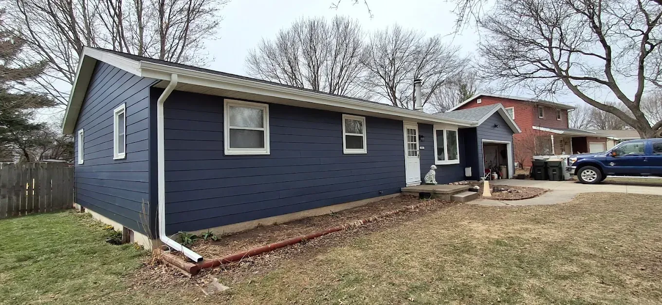 Blue house with white trim, two windows, and a tree in the background.