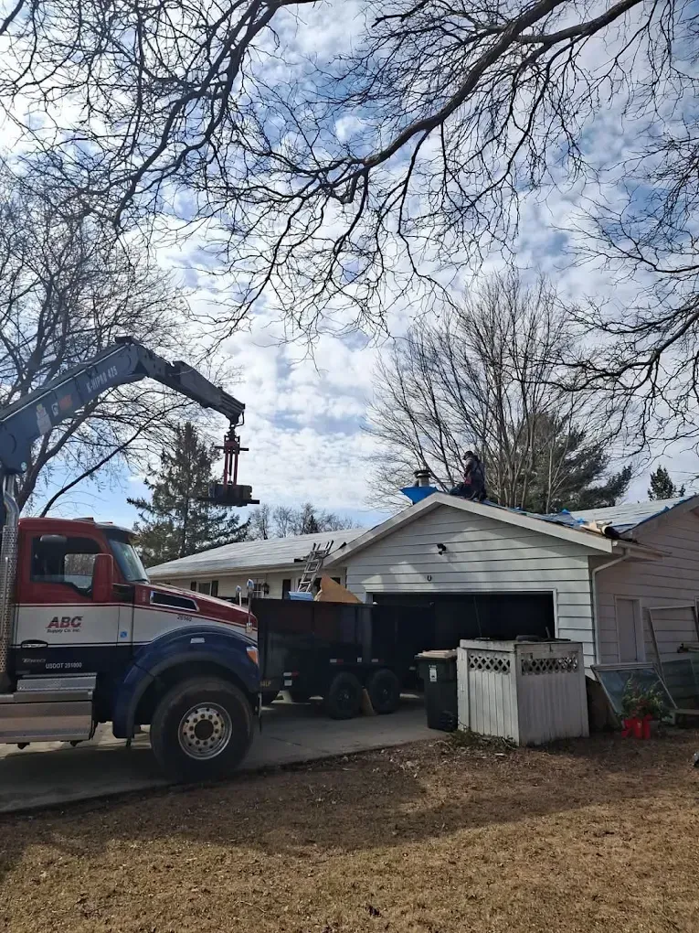 Crane lifting materials to a roof where two workers are standing; blue sky.