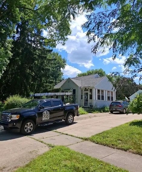Black truck parked in front of a white house with a car in the driveway, under a blue sky.
