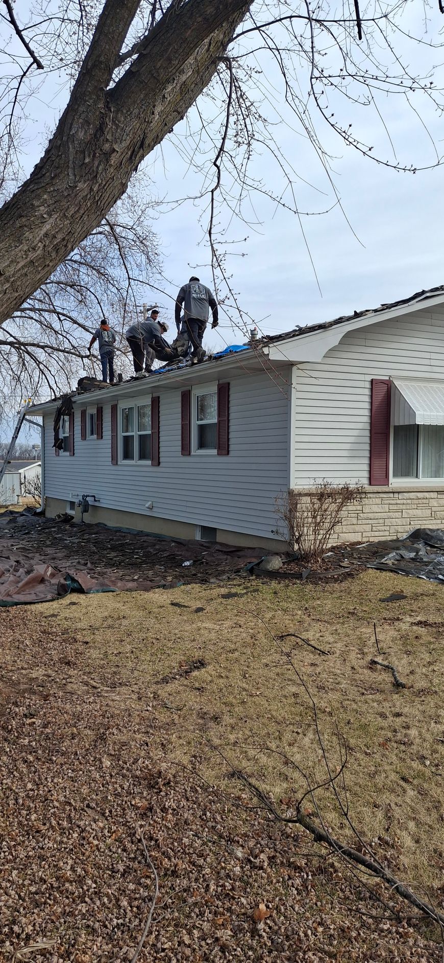Three roofers on the roof of a white house with red shutters, working on roof repair.