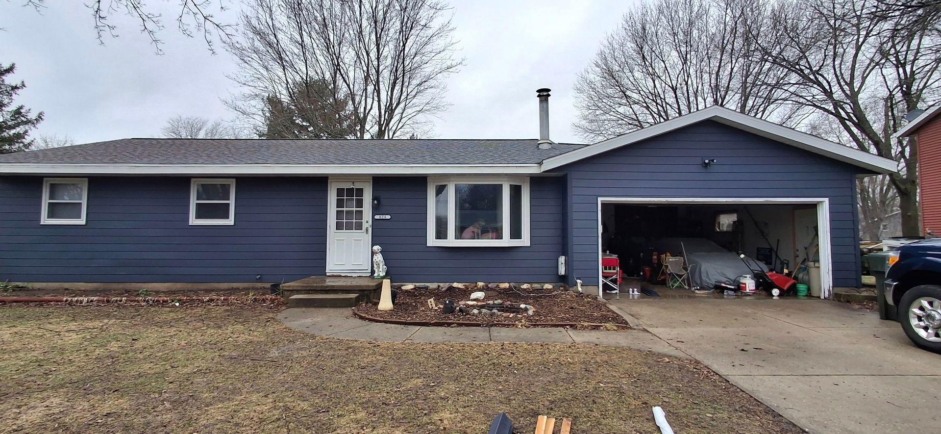 Blue-sided house with garage. Brown yard. Overcast sky.