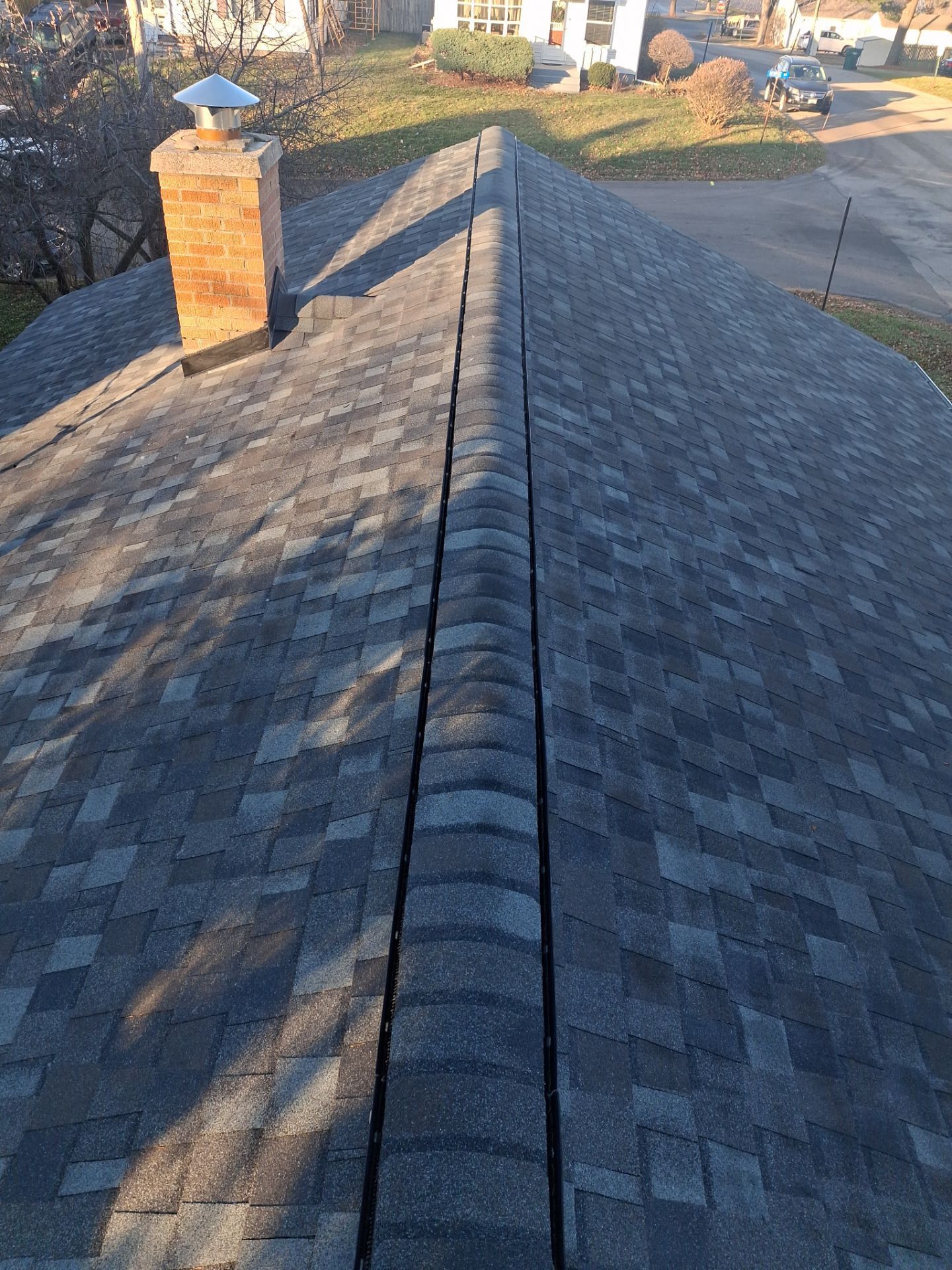 View from a rooftop: Dark asphalt shingles with a central trough and brick chimney in daylight.