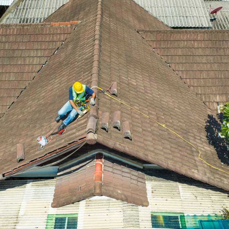 Roofer in yellow hard hat and safety vest on a tile roof, attached to a safety rope, working.