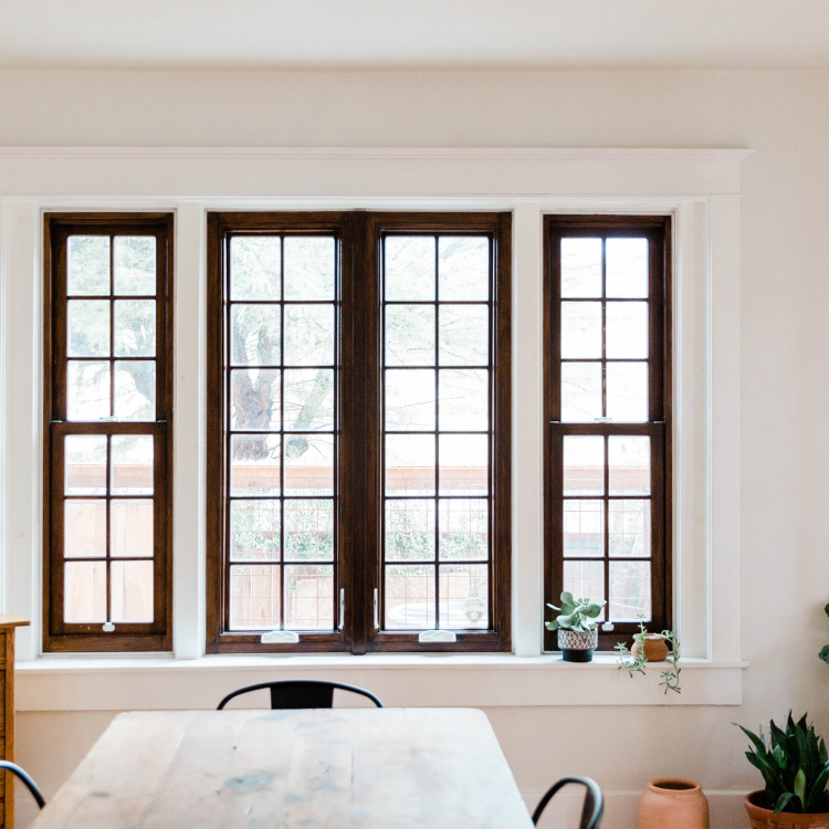 Three dark-framed windows in a cream-colored room, above a table and plants.