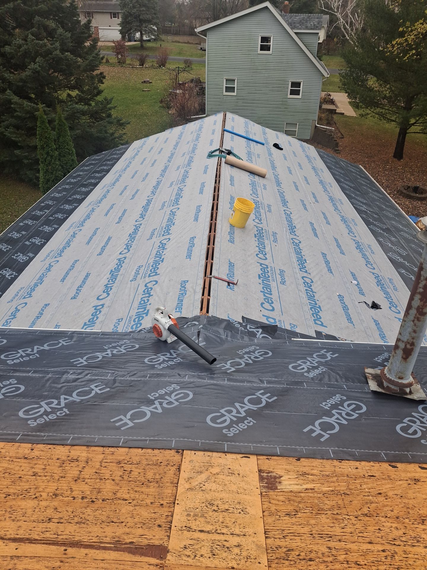 Roof under construction: black underlayment and blue paper, tools scattered.